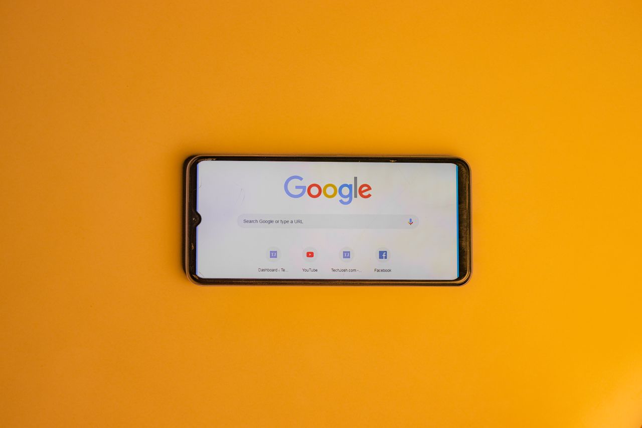 Smartphone displaying Google search page on a vibrant yellow background.